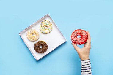 Kadın eli mavi arka planda donut tutuyor. Şekerleme dükkanı, hamur işleri, kahve dükkanı. Pankart. Düz yatış, üst görünüm