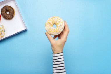 Kadın eli mavi arka planda donut tutuyor. Şekerleme dükkanı, hamur işleri, kahve dükkanı. Pankart. Düz yatış, üst görünüm