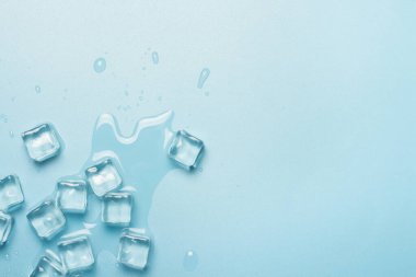 Mavi zemin üzerinde su olan buz küpleri. İçkiler için buz konsepti. Pankart. Düz yatış, üst görünüm