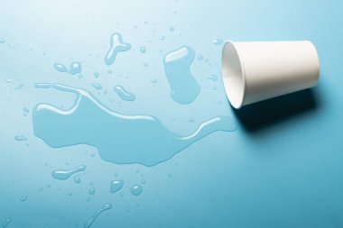 Mavi arka planda dökülmüş su bardağı. Soyut ışık. İçkiler için buz konsepti. Pankart. Düz yatış, üst görünüm