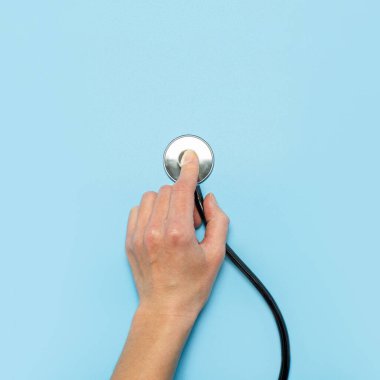 Kadının elinde mavi arka planda steteskop var. Konsept doktor, doktor randevusu, virüs, tedavi, teşhis. Düz yatış, üst görünüm