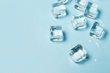 Mavi zemin üzerinde su olan buz küpleri. İçkiler için buz konsepti. Pankart. Düz yatış, üst görünüm