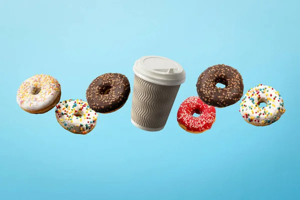 Donuts voando no ar e xícara de papel de café em um fundo azul. Padaria, conceito de cozedura. Levitação. Banner — Fotografia de Stock