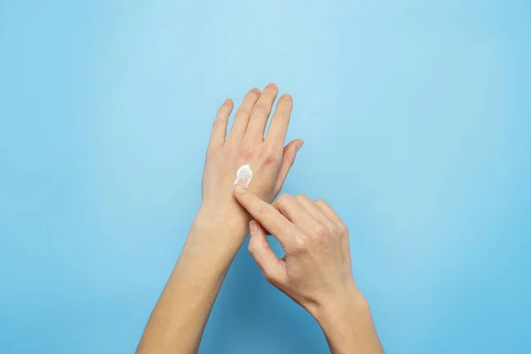 Women's hands. Woman smears cream on her hand on a blue background. The concept of cosmetics, skin care, lotion, makeup, spa. Banner Flat lay, top view — 스톡 사진