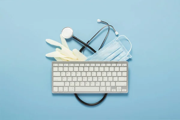 Keyboard, medical stethoscope, latex gloves and a protective mask on a blue background. Concept medicine, hospital, safety, epidemic, doctor\'s call, online, consultation. Banner. Flat lay, top view
