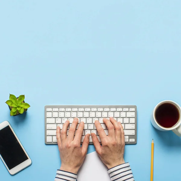 Woman works in the office on a blue background.Only hands Concept workspace, working at a computer, freelance, design. phone, flower, pencil. Banner. Flat lay, top view — Stock Photo, Image