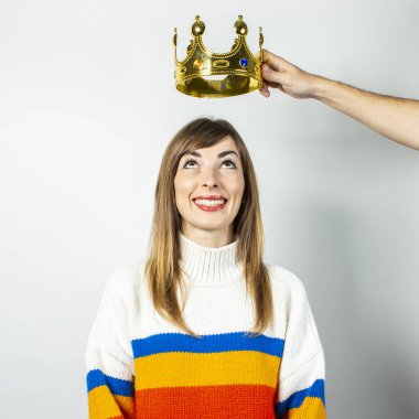 El, beyaz arka planda gülümsemesi ve süveteri olan genç bir kadının üzerinde bir taç tutuyor. Arzu kavramı, planlama, hayal, ego. Pankart