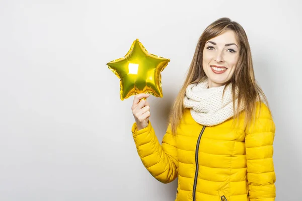 Woman with smile in a yellow jacket and a scarf holds a star air balloon on a white background. Concept of a holiday, celebration, party, new year. Banner