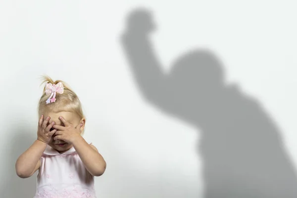 El niño se cubre la cara con las manos sobre un fondo claro con la sombra de un hombre atacante. Concepto de miedo, miedo, violencia doméstica, juego de cerraduras — Foto de Stock