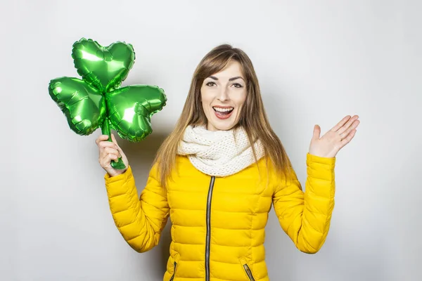 Γυναίκα με ένα χαμόγελο σε ένα κίτρινο σακάκι και ένα μαντήλι κρατά ένα μπαλόνι τριφύλλι σε λευκό φόντο. Έννοια των διακοπών, γιορτή, κόμμα, Ημέρα του Αγίου Πατρικίου, Ιρλανδία. Μπάνερ — Φωτογραφία Αρχείου