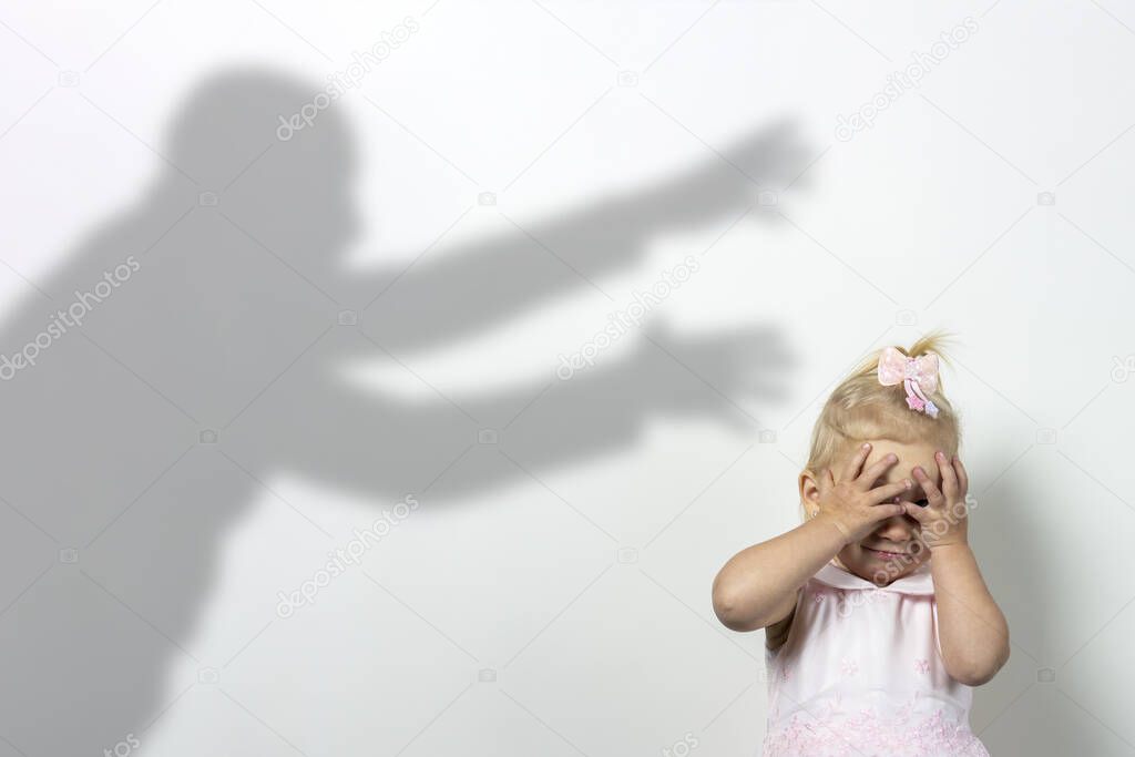 Little child covers his face with his hands on a light background with the shadow of an attacking man. Concept of fear, fear, domestic violence, the game of locks