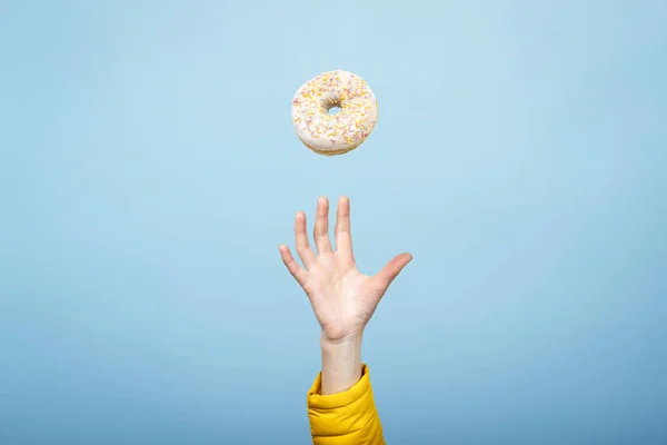 Mão pegar um donut com gelo. Fundo de papelão azul. Conceito de cozimento, feito à mão. Deitado plano, vista superior — Fotografia de Stock