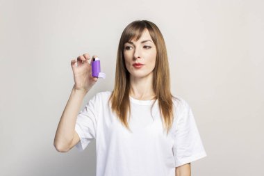 Üzgün genç bir kadın elinde astım spreyini tutuyor ve arka plandaki solunum cihazına bakıyor. Pankart. Daha kolay nefes alma, astım tedavisi, gırtlak, soluk borusu....