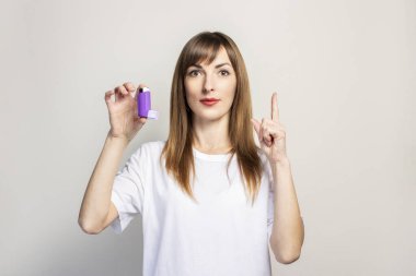 Genç bir kadın elinde bir astım spreyi tutuyor, arka planda baş parmak tutuyor. Pankart. Daha kolay nefes alma, astım tedavisi, gırtlak, soluk borusu....