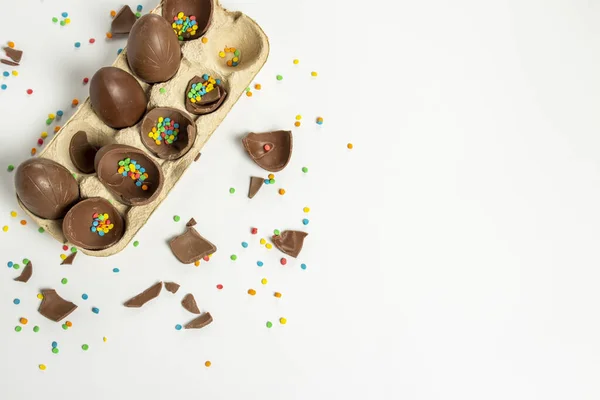 Tray with broken Easter chocolate eggs and multi-colored sweet candy decorations on a light background. Easter concept, easter treats, bunny. Banner. Flat lay, top view.