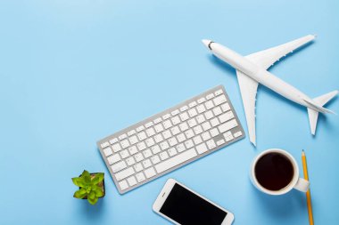 Klavye, çiçek, uçak, çay ya da kahve bardağı, boş bir çarşaf ve mavi arka planda bir kalem. Seyahat planı, online uçak biletleri, uçak biletleri. Pankart. Düz yatış, üst görünüm.