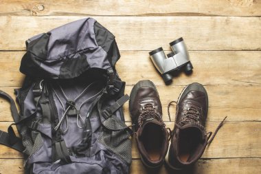 İz sürme botları, sırt çantası, dürbün, ahşap arka planda kamp malzemeleri. Yürüyüş, turizm, kamp, dağlar, orman konsepti. Pankart. Düz yatış, üst görünüm.