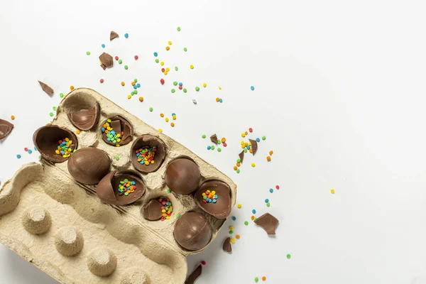 Tray with broken Easter chocolate eggs and multi-colored sweet candy decorations on a light background. Easter concept, easter treats, bunny. Banner. Flat lay, top view.