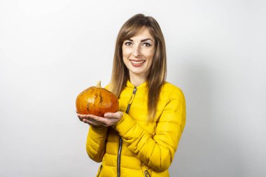 Sarı ceketli güzel genç kız arka planda bir balkabağı tutuyor. Cadılar Bayramı konsepti, kutlama.