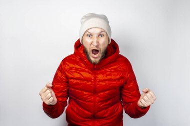 Genç adam kırmızı ceketli ve arka planda şapkası olan çığlıklar atıyor. Stres ve öfke kavramı.