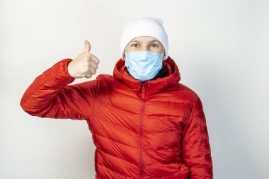 Yüzünde tıbbi bir maske olan kırmızı ceketli genç adam arka planda birinci sınıf bir hareket sergiliyor. Soğuk algınlığı, virüs, bulaşıcı hastalıklar.