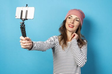 Genç kadın blogcu mavi arka planda telefonla kendi fotoğraflarını çekiyor. Kavram hikayesi, vlog, selfie, blog.