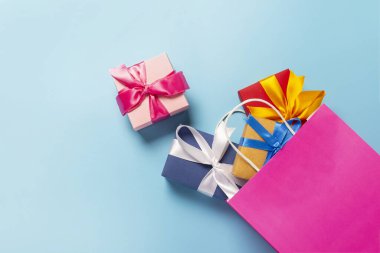 from a pink bag packing boxes fall out on a blue background. Gift bag and boxes. Concept of holidays, shopping, sale, discounts. Banner. Top view, flat lay. clipart