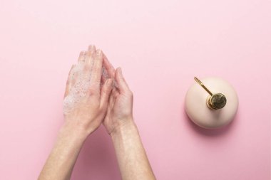 Sabunlu kadın elleri ve pembe arka planda dezenfektanlı bir şişe. Antiseptik, el hijyeni ve el tedavisi kavramı. Üst manzara, düz uzanma.