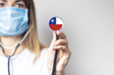 Tıbbi maskeli kadın doktor arka planda steteskop tutuyor. Şili bayrağı eklendi. Tıp, ilaç seviyesi, virüs, salgın hastalık.
