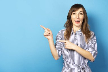 Elbise giymiş güzel bir kız parmaklarını yana doğru gösteriyor ve doğrudan kameraya bakıyor. Yaz kavramı, dinlenme, seyahat.