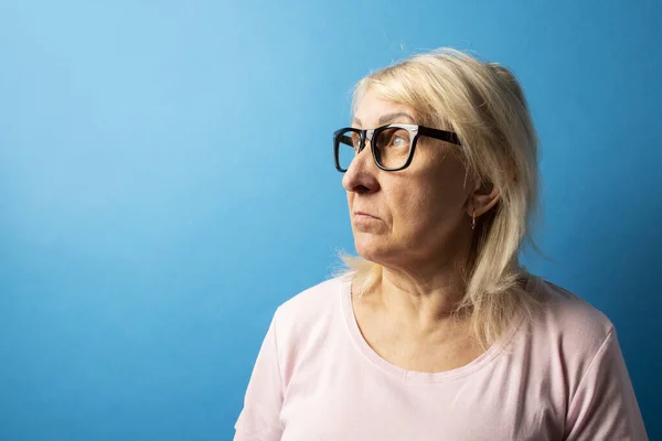 Oude Vrouw Met Bril Kijkt Weg Een Blauwe Geïsoleerde Achtergrond — Stockfoto