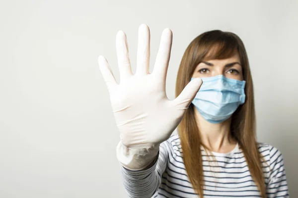 Young woman in a protective medical mask and latex gloves holds her hand and shows the viewer on a light isolated background. Concept of coronavirus, clean hands, no virus, stop. Banner. copy space.