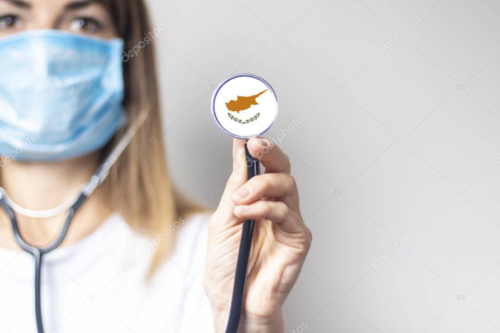 female doctor in a medical mask holds a stethoscope on a light background. Added flag of Cyprus. Concept medicine, level of medicine, virus, epidemic.