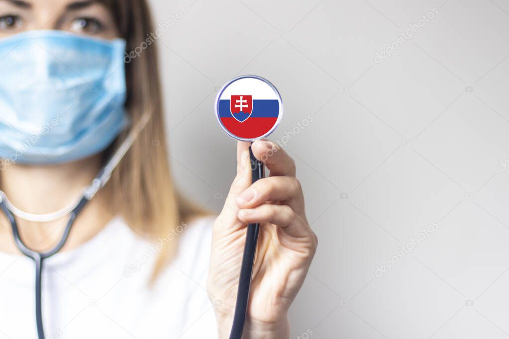 female doctor in a medical mask holds a stethoscope on a light background. Added flag of Slovakia. Concept medicine, level of medicine, virus, epidemic.