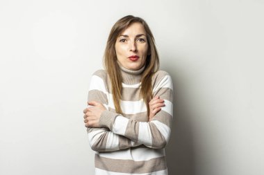 Çizgili süveter giyen genç ve arkadaş canlısı bir kadının portresi izole bir arka planda kendine şaşırmış bir yüzle sarıldı. Duygusal bir yüz. Jest soğuk, sürpriz, korkutucu.