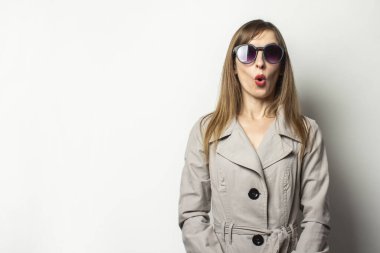 Klasik ceketli ve güneş gözlüklü, izole edilmiş ışık arka planında şaşırmış bir kadın portresi. Duygusal bir yüz. Klasik tarz, Fransız kadın, sürpriz, şok.