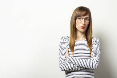 Uzun kollu ve kolları göğsünde çaprazlanmış gözlüklü, izole bir arka planda ciddi bir yüzü olan dost canlısı genç bir kadının portresi. Duygusal yüz..