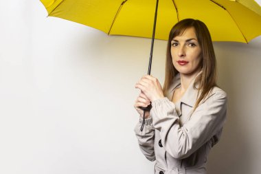 Sarı bir şemsiyenin altında, arka planda, klasik ceketli, dost canlısı genç bir kadının portresi. Duygusal bir yüz. Kötü hava, yağmur, hava tahmini.