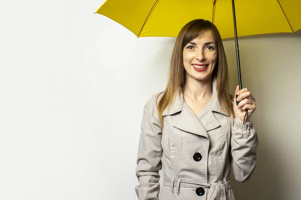 Portrait Young friendly woman in a classic jacket with a smile under a yellow umbrella on an isolated light background. Emotional face. Bad weather, rain, weather forecast.