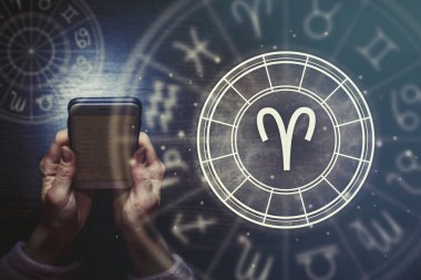 Kadın eller, yıldızlı gökyüzünün arka planında Koç burcuyla birlikte bir telefon ve astrolojik bir çember tutuyorlar. Yıldız falı uygulaması.