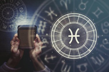 Dişi eller, yıldızlı gökyüzünün arka planında balık burcu olan bir telefon ve astrolojik bir çember tutuyorlar. Yıldız falı uygulaması.
