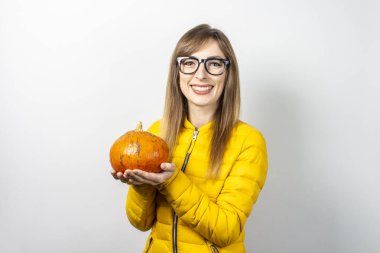 Sarı ceketli güzel genç kız arka planda bir balkabağı tutuyor. Cadılar Bayramı konsepti, kutlama.