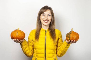 Sarı ceketli mutlu genç kız arka planda iki balkabağı tutuyor. Cadılar Bayramı konsepti, sonbahar, kutlama.