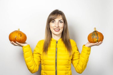 Sarı ceketli güzel genç kız arka planda iki balkabağı tutuyor. Cadılar Bayramı konsepti, sonbahar, kutlama. 