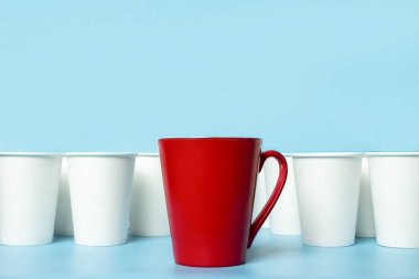 Kırmızı bardak mavi arka planda beyaz kağıt bardaklarla çevrili. Konsept patronu, eşsiz, dost canlısı takım. Boşluğu kopyala.