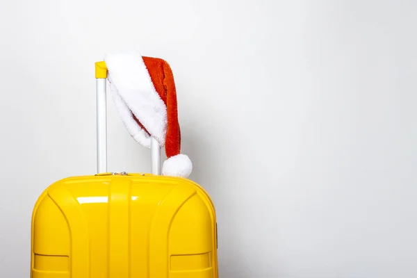 Yellow Plastic Suitcase Wearing Red Santa Claus Hat Light Background — Stock Photo, Image