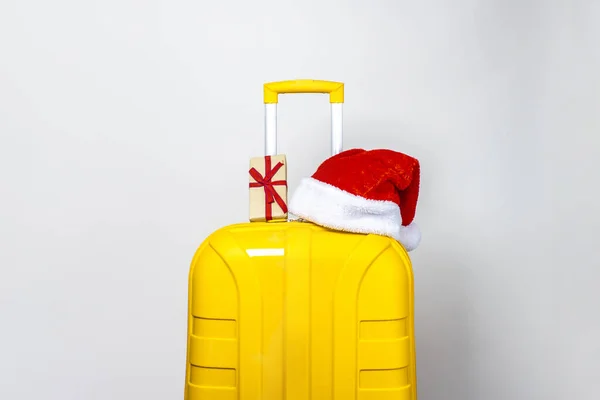 黄色のプラスチック製のスーツケースには贈り物があり 薄い背景に赤いサンタクロースの帽子をかぶっています — ストック写真