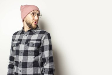 Şapkalı, ekose gömlekli ve gözlüklü genç bir adamın portresi izole bir arka plana bakıyor. Duygusal yüz..