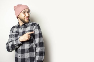 Şapkalı, ekose gömlekli ve gözlüklü genç bir adamın portresi izole bir arka plana bakıyor. Duygusal yüz..