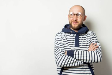 Kapüşonlu gözlüklü sakallı kel bir gencin portresi izole edilmiş bir ışık arka planına bakıyor. Duygusal yüz..